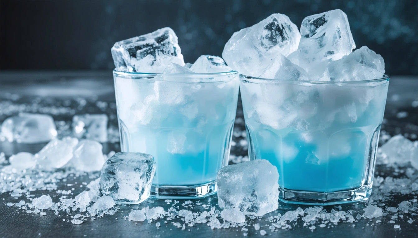 Two glasses filled with blue liquid and topped with ice cubes, surrounded by scattered ice on a dark surface
