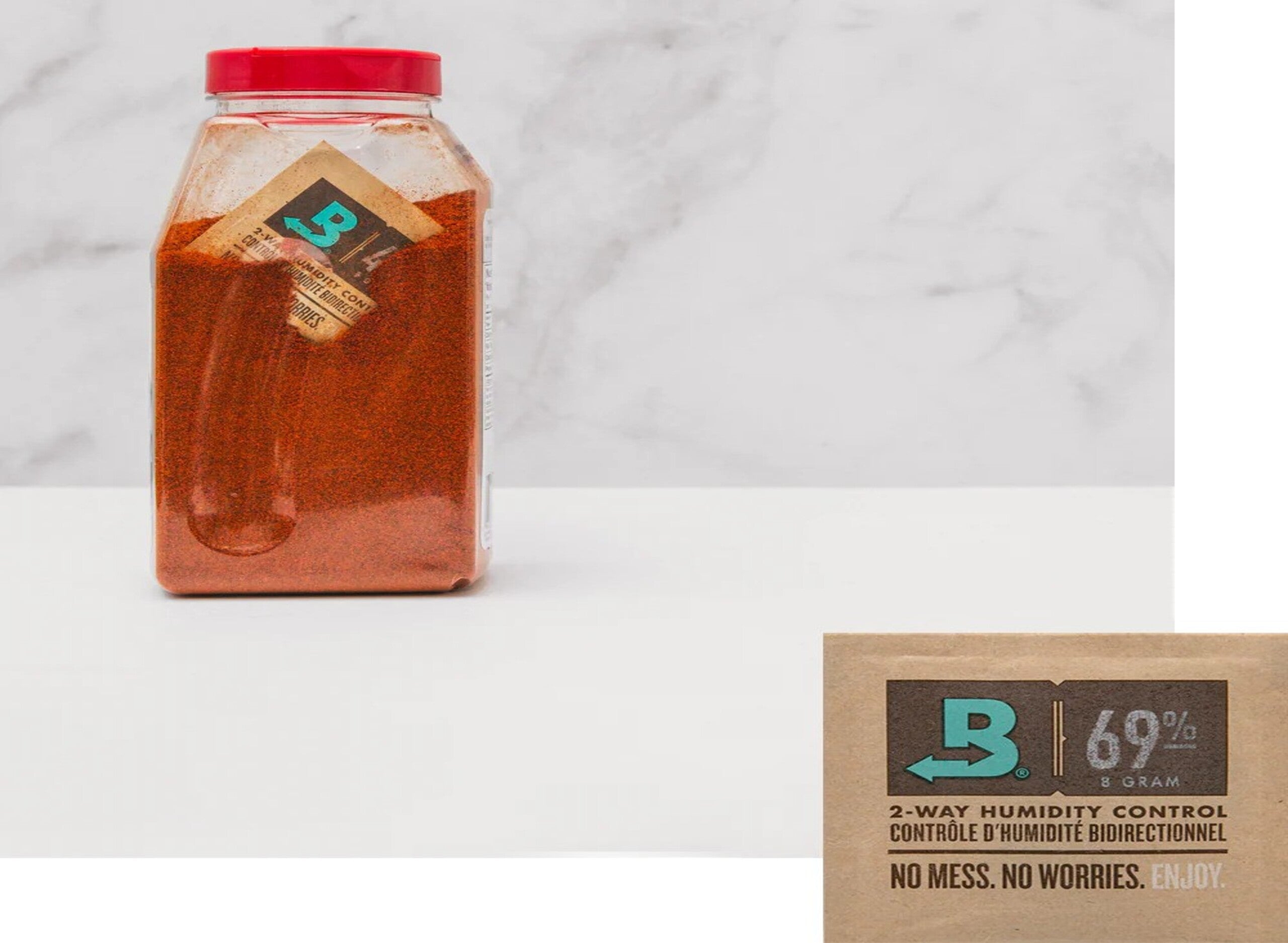Hand placing cannabis bud into glass jar, surrounded by dropper bottles and small bowl of buds on wooden surface, green background